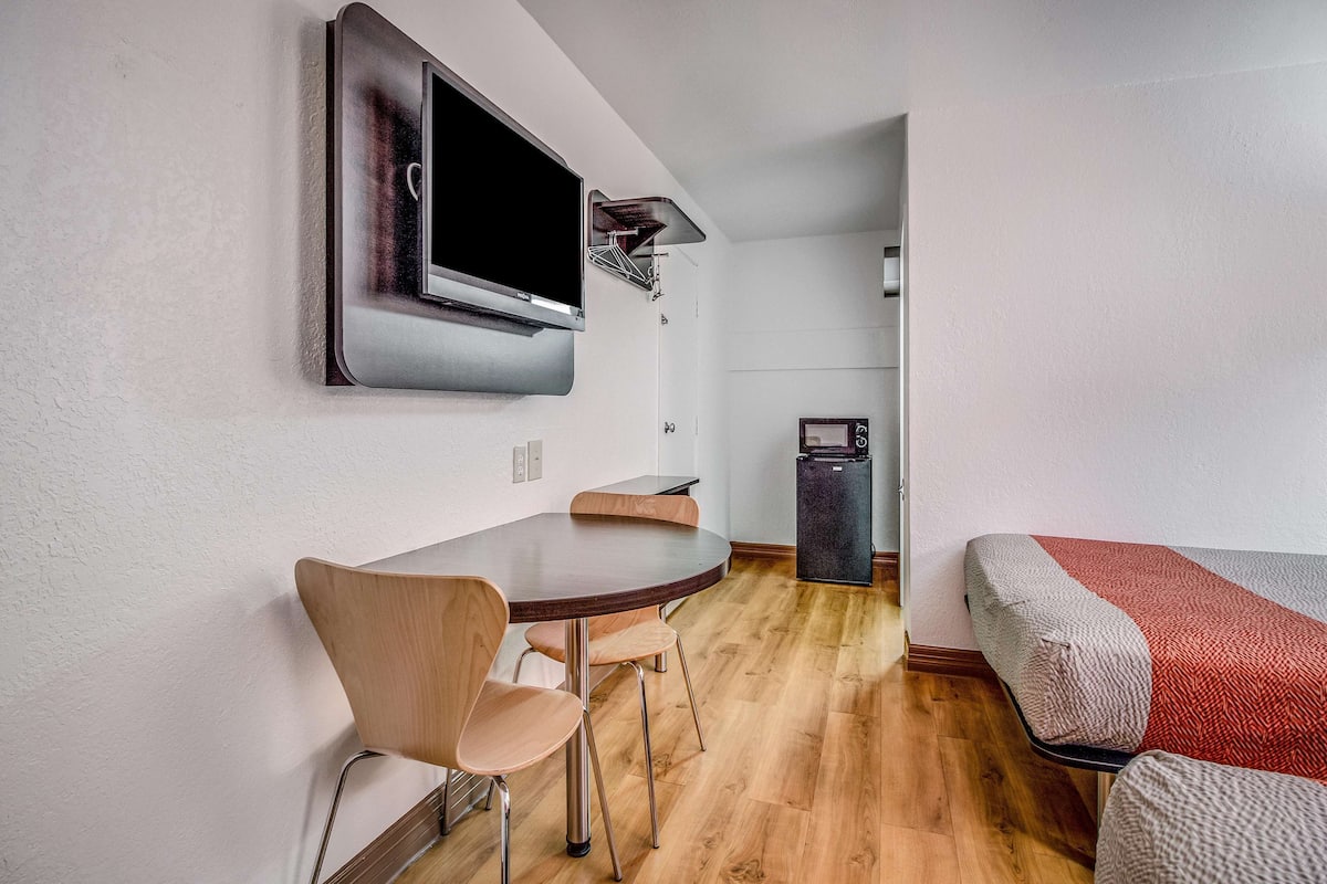 A modern room with a wooden dining table, a TV mounted on the wall, and a bed with a red and white striped blanket.