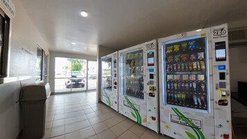 Varias máquinas expendedoras en un área comercial con piso de baldosas y un bote de basura a la izquierda.
