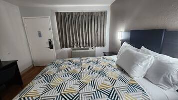 Ein Hotelzimmer mit Bett, Nachttisch, Tür und einem Fenster mit Vorhängen.