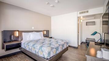 Une chambre d’hôtel moderne avec un grand lit, des tables de chevet avec des lampes, un bureau et une kitchenette.