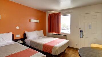 A hotel room with two beds, a window with curtains, a table, and a door.