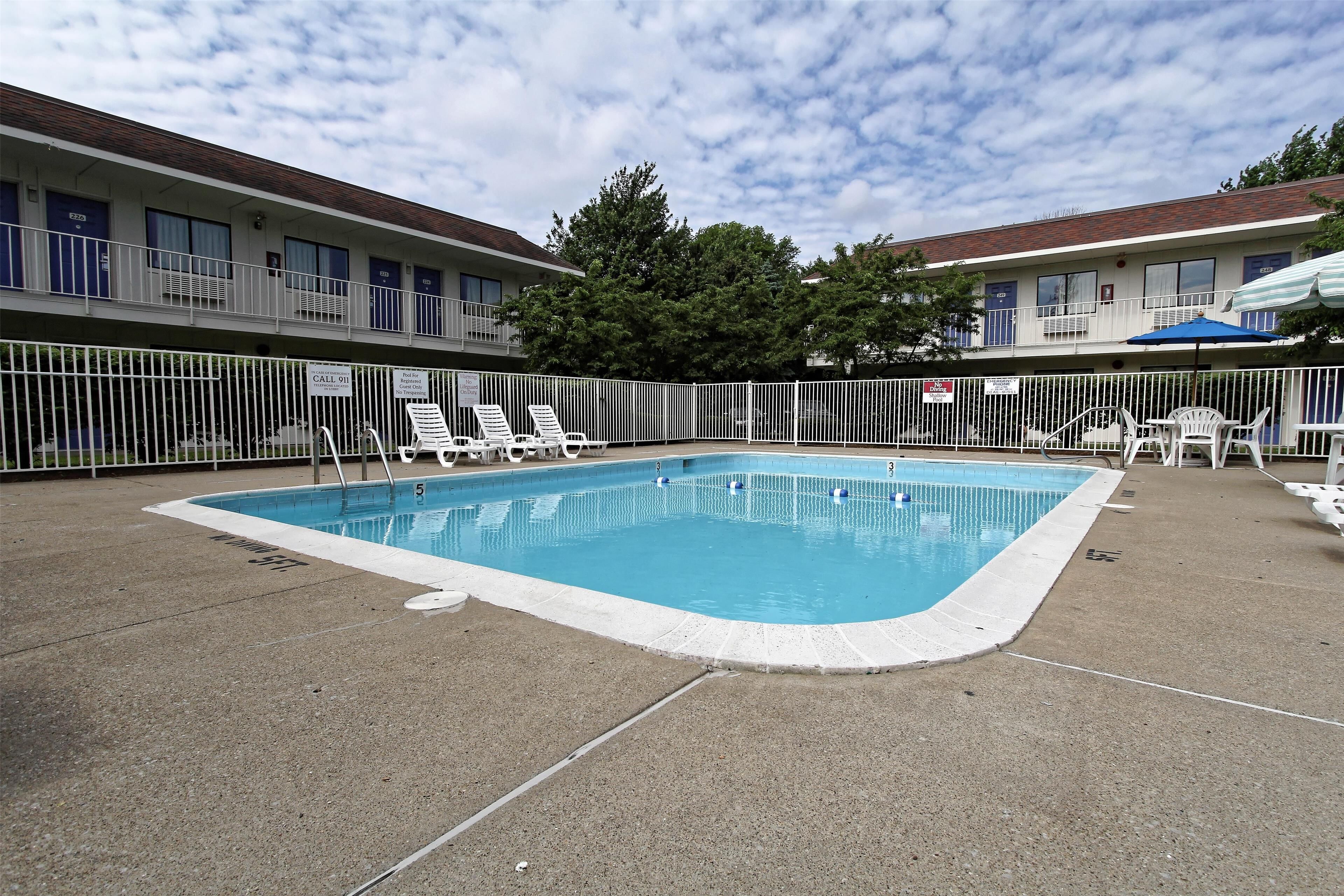 A swimming pool with lounge chairs and a fenced area, surrounded by motel buildings.