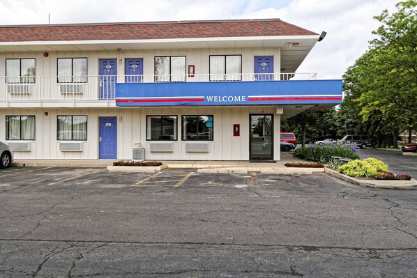 A motel with a 'WELCOME' sign, a parking lot, and a small garden area.