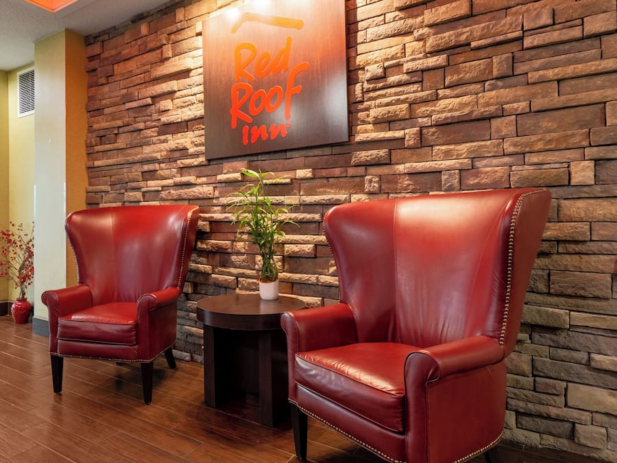 Lobby de um Red Roof Inn com duas poltronas de couro, uma pequena mesa e um vaso de planta.