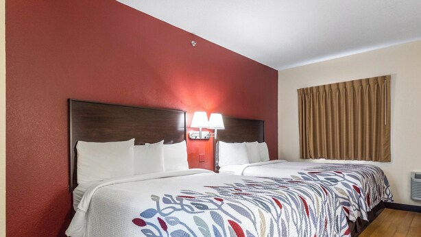 A hotel room with a large bed, a nightstand with a lamp, and a window with curtains. - Red Roof Inn Georgetown, IN - Louisville West (Georgetown)