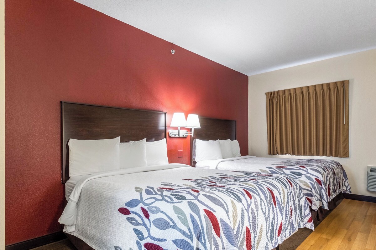 A hotel room with a large bed, a nightstand with a lamp, and a window with curtains.