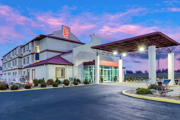 A hotel with a red roof sign, a covered entrance, and a parking lot.