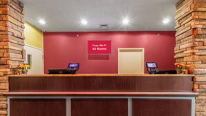 Un comptoir d’accueil avec un mur rouge, deux ordinateurs et un panneau indiquant que le Wi-Fi est disponible gratuitement dans toutes les chambres.