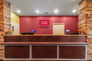 A reception desk with a red wall, two computers, and a sign indicating free Wi-Fi in all rooms.