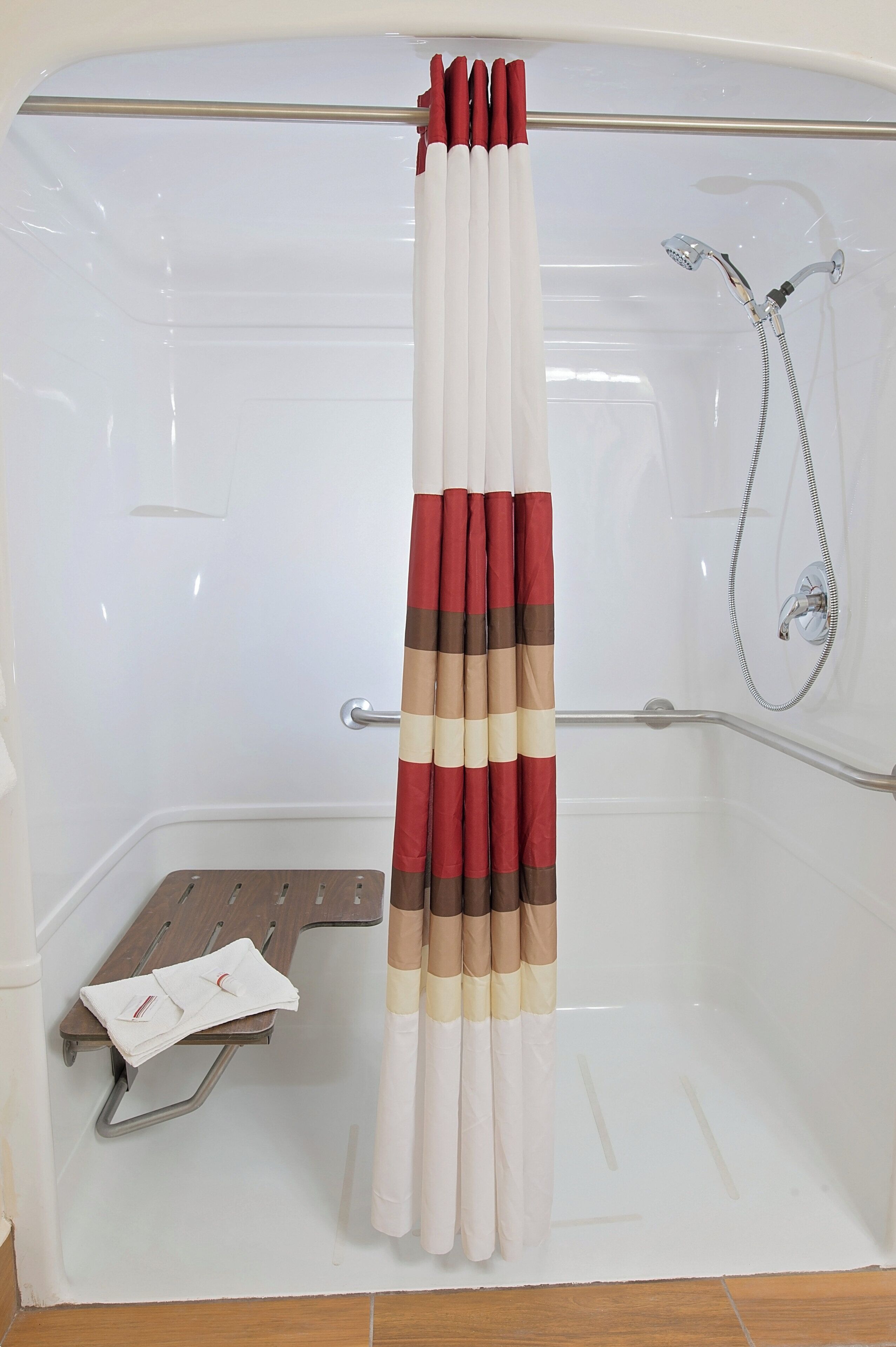Un espace douche avec un rideau de douche blanc, une douchette à main et un porte-serviettes avec des serviettes pliées.