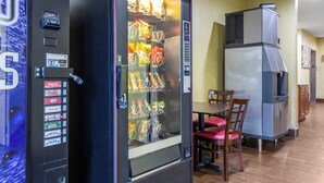 A vending machine with snacks and drinks, a table with chairs, and a refrigerator in a room. - Red Roof Inn Georgetown, IN - Louisville West (Georgetown)