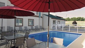 Un espace aménagé au bord de la piscine, avec des chaises longues et des tables, un parasol rouge et une piscine.