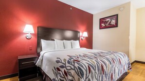 Une chambre d’hôtel avec un lit, deux lampes de chevet, une table de chevet, un tableau encadré au mur et un mur d’accent de couleur rouge.