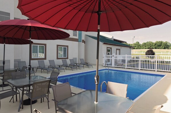 A poolside area with lounge chairs and tables, a red umbrella, and a pool. - Red Roof Inn Georgetown, IN - Louisville West (Georgetown)