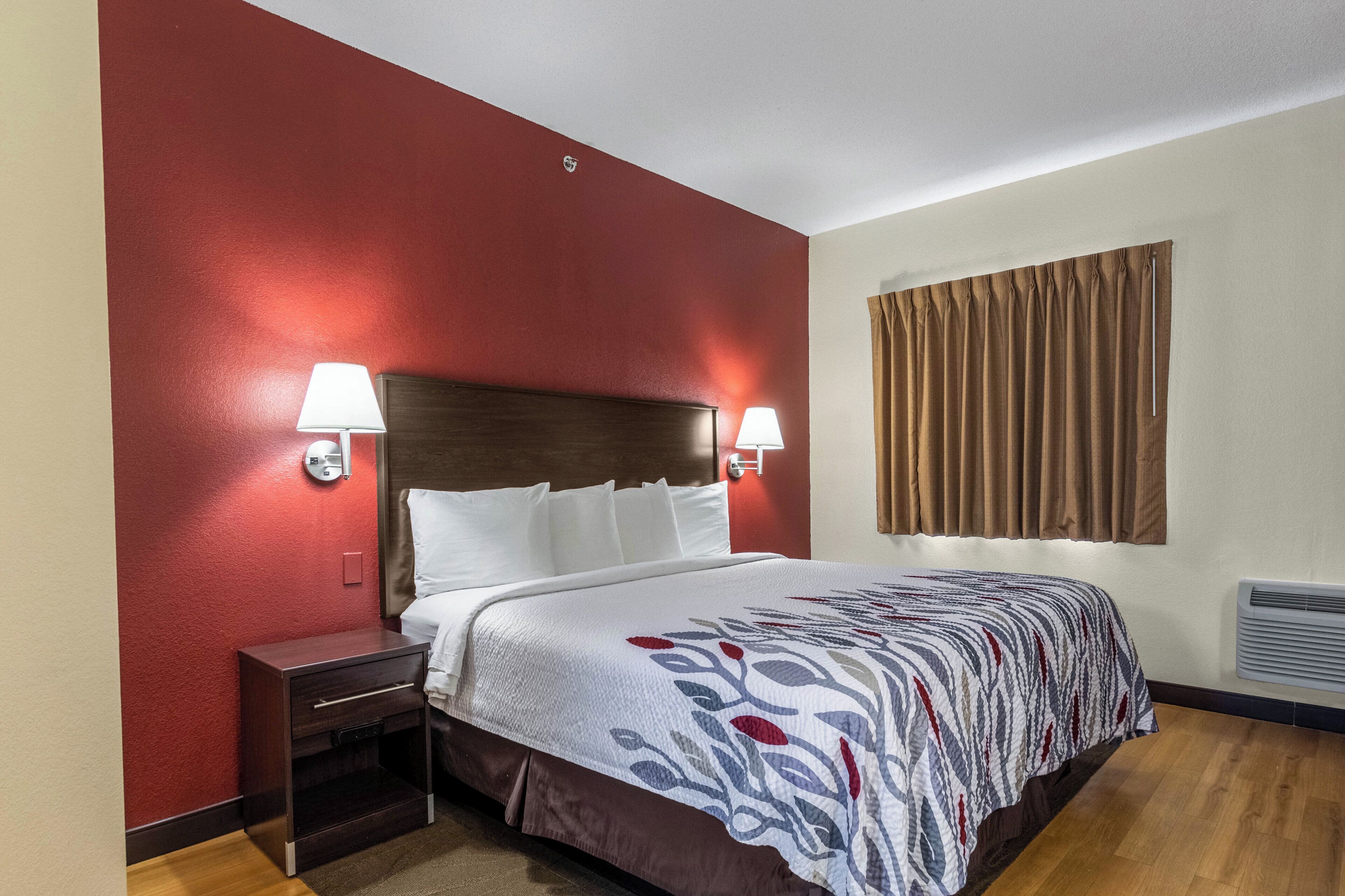 Ein Hotelzimmer mit Bett, Nachttischen, einem Fenster mit Vorhängen und Wandlampen.