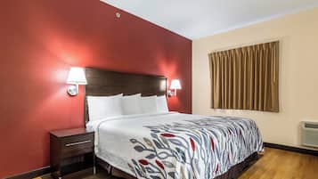 Habitación de hotel con cama, mesita de noche, dos lámparas fijadas a la pared, una ventana con cortinas y un calentador de pared.