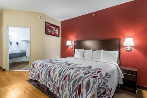 A hotel room with a bed, two bedside lamps, a nightstand, and a door leading to a bathroom. - Red Roof Inn Georgetown, IN - Louisville West (Georgetown)