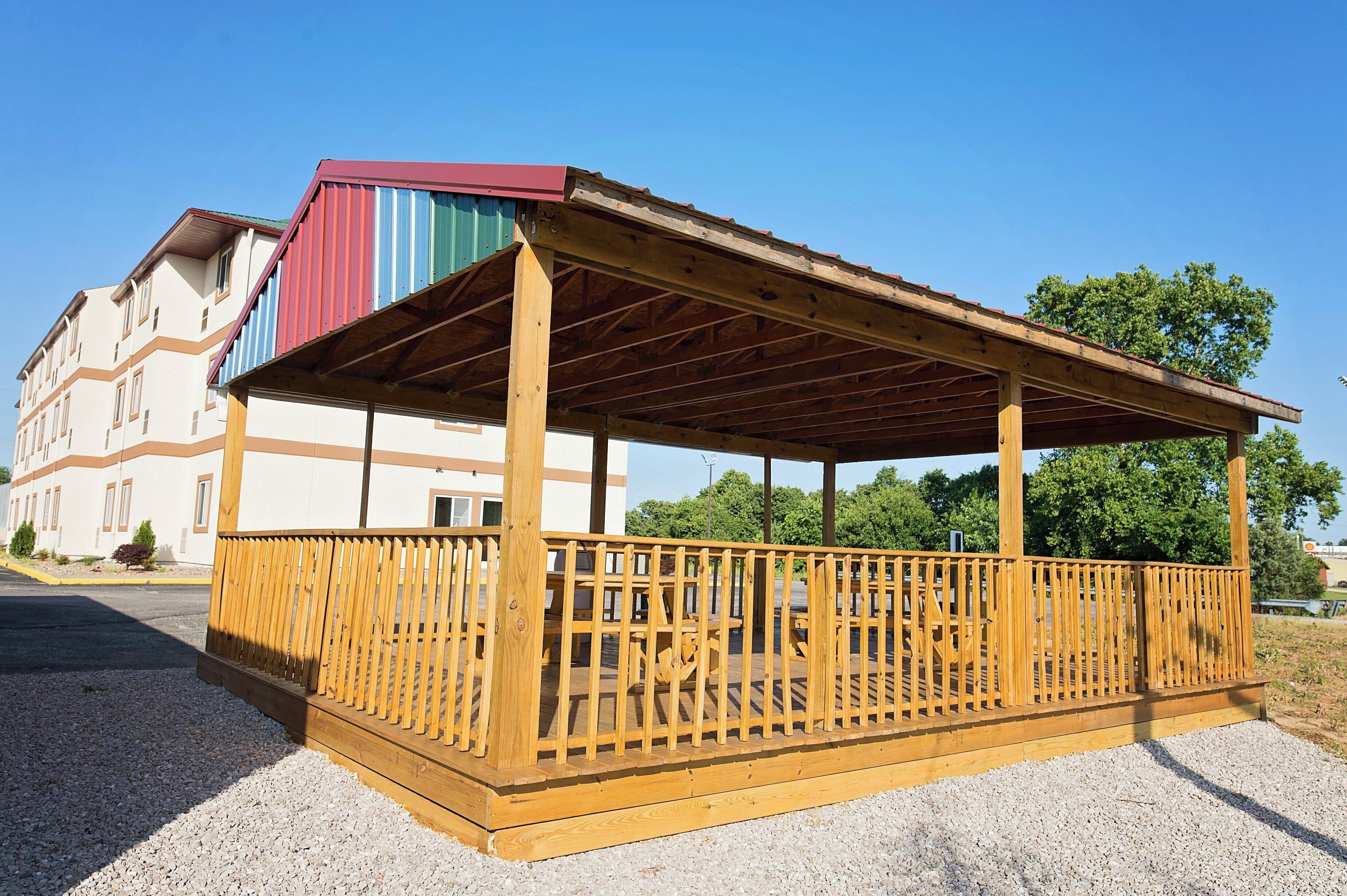 Un pavillon en bois, doté d’un toit à pente, entouré d’une clôture en bois, et un bâtiment avec un auvent rayé en arrière-plan.