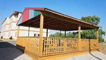 Un pavillon en bois, doté d’un toit à pente, entouré d’une clôture en bois, et un bâtiment avec un auvent rayé en arrière-plan.