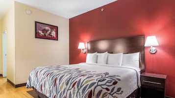 Ein Hotelzimmer mit Bett, Nachttischlampen, einem Nachttisch, einem gerahmten Bild an der Wand und einer Tür links.