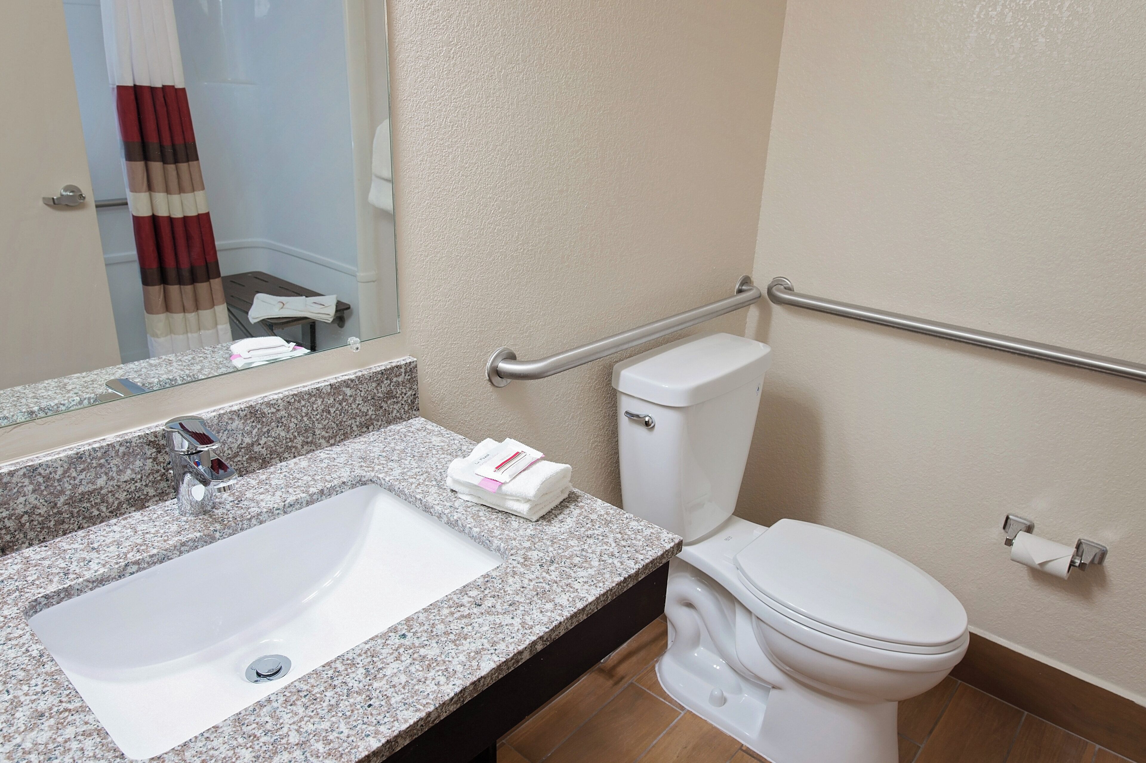 A bathroom with a granite countertop sink, a toilet, and a handrail.