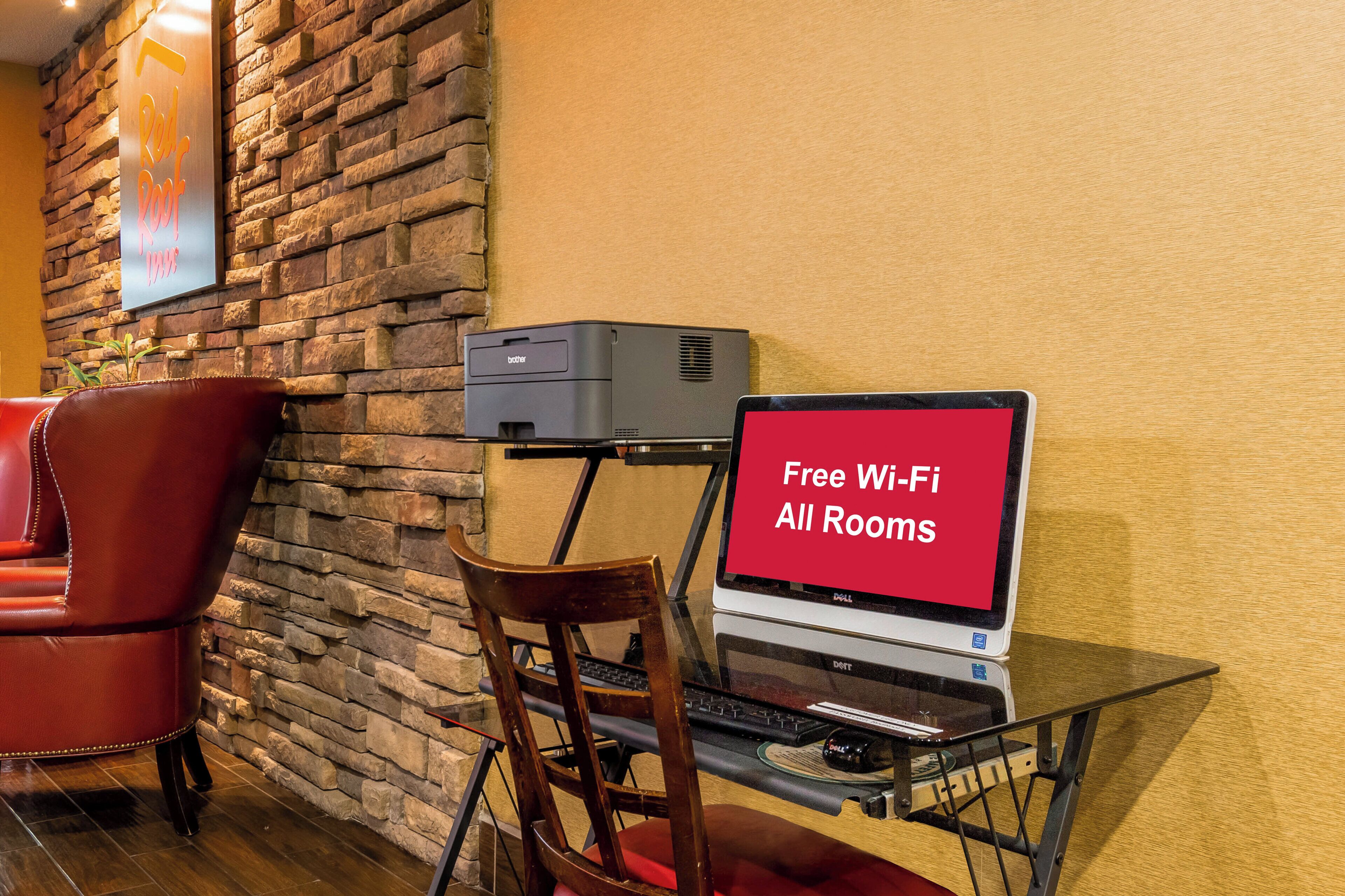 Ein Hotelzimmer mit Steinsturz, einem roten Ledersessel, einem Schreibtisch mit Laptop und einem Schild, das kostenloses WLAN in allen Zimmern anbietet.