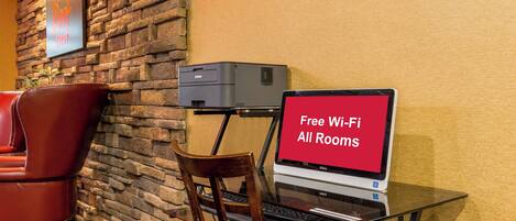 A hotel room with a stone wall, a red leather chair, a desk with a laptop, and a sign offering free Wi-Fi in all rooms.