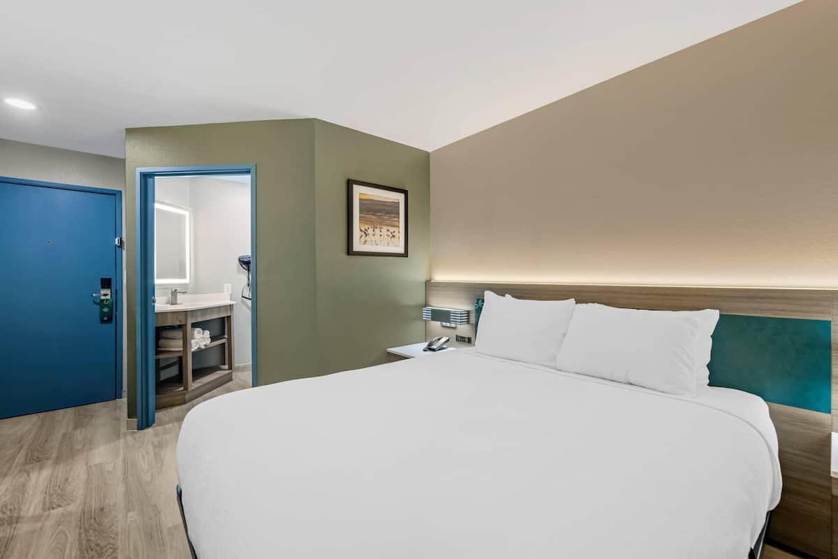 A hotel room with a large bed, a nightstand, a bedside table, a mirror, and a wardrobe.