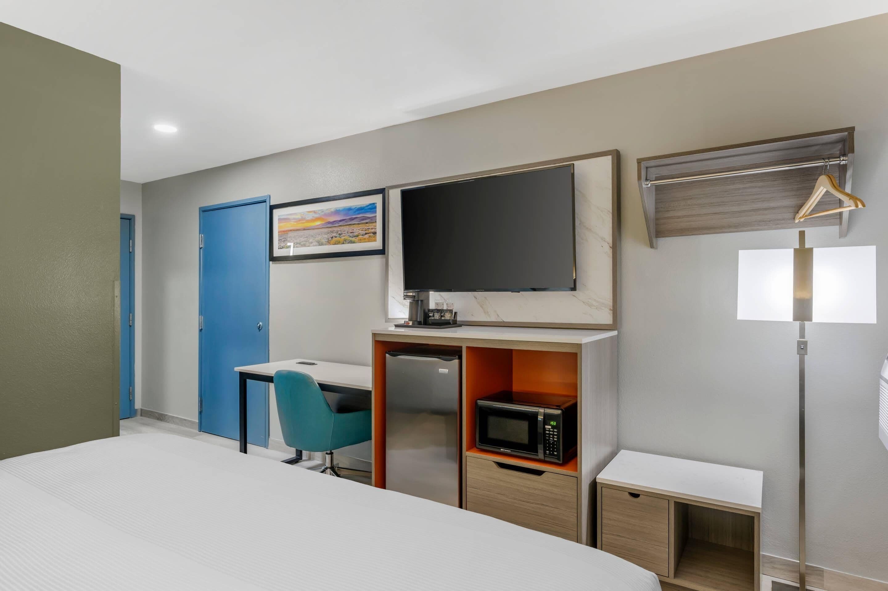 Una habitación de hotel con cama, escritorio y silla, microondas, televisión, armario y perchero.