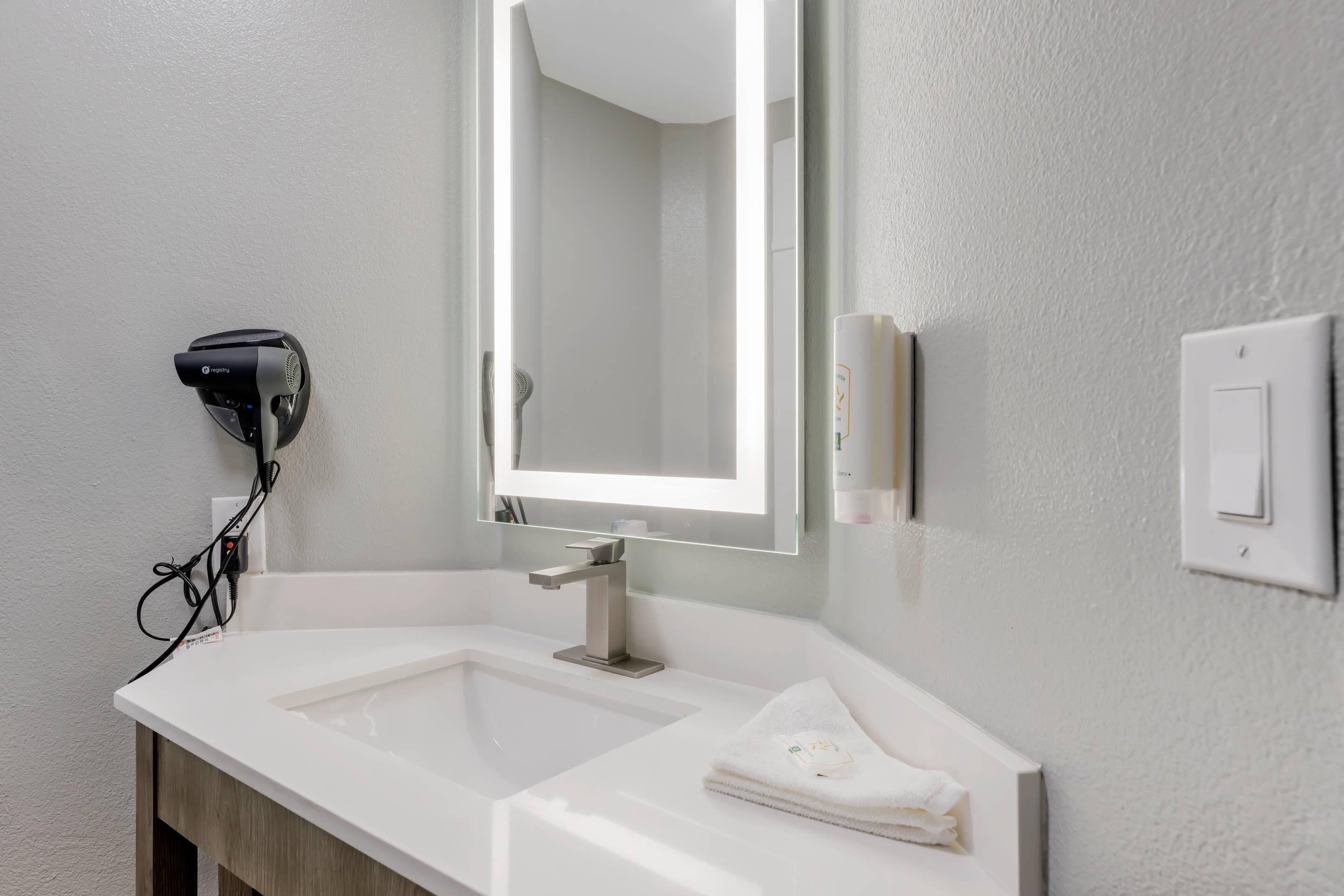 Un bagno moderno con un lavandino bianco, uno specchio grande e un asciugacapelli a parete.