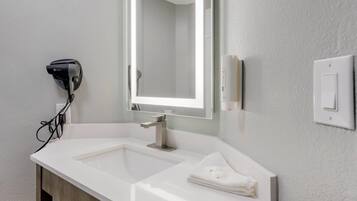 Un bagno moderno con un lavandino bianco, uno specchio grande e un asciugacapelli a parete.