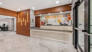 A modern reception area with a wooden panel design, a marble floor, and a wall decorated with various artworks and a sign that reads "Quality by Gracey." - Quality Inn Ruidoso (Ruidoso)