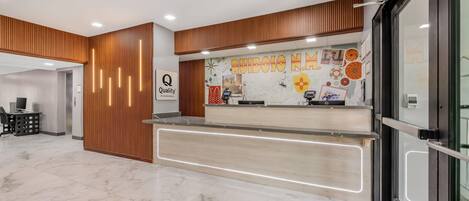 A modern reception area with a wooden panel design, a marble floor, and a wall decorated with various artworks and a sign that reads "Quality by Gracey."
