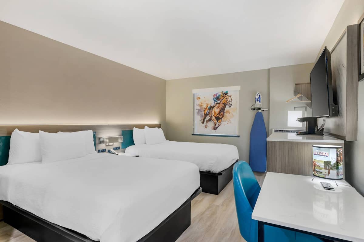 A hotel room with two beds, a desk, a TV, and a painting on the wall.