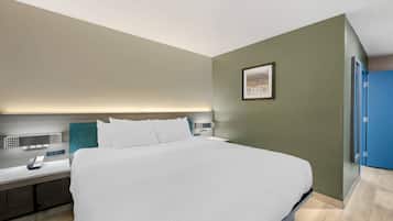 A modern hotel room with a large bed, a bedside table with a phone, a nightstand with a lamp, and a framed picture on the wall.