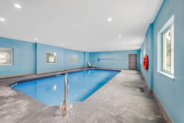 A large indoor swimming pool with a blue tiled floor, a metal ladder, and a lifebuoy on the wall. - Quality Inn Ruidoso (Ruidoso)