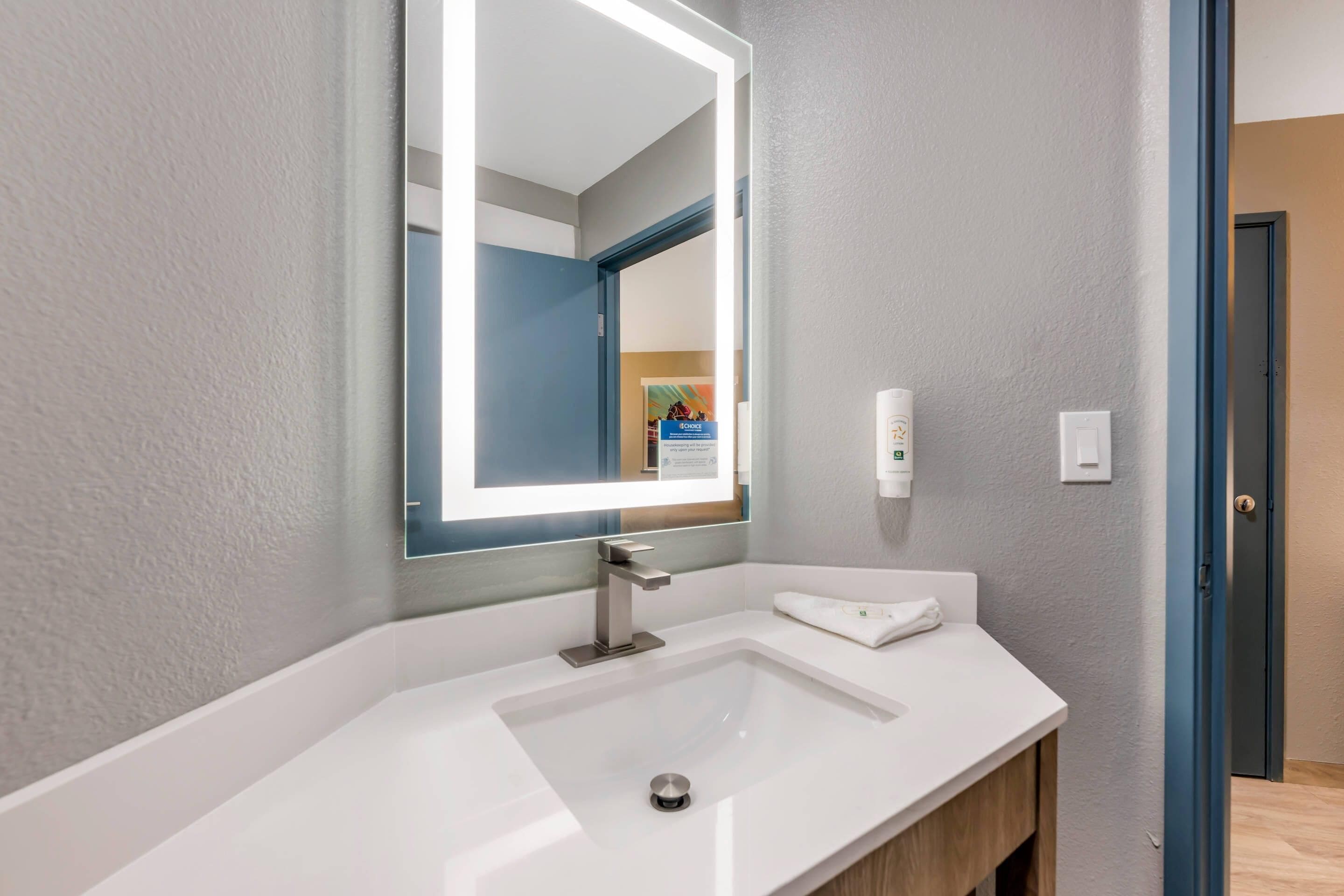 Un baño moderno con un lavabo blanco, un espejo grande con iluminación integrada y un perchero para toallas.