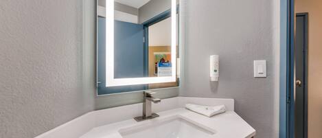 Un baño moderno con un lavabo blanco, un espejo grande con iluminación integrada y un perchero para toallas.
