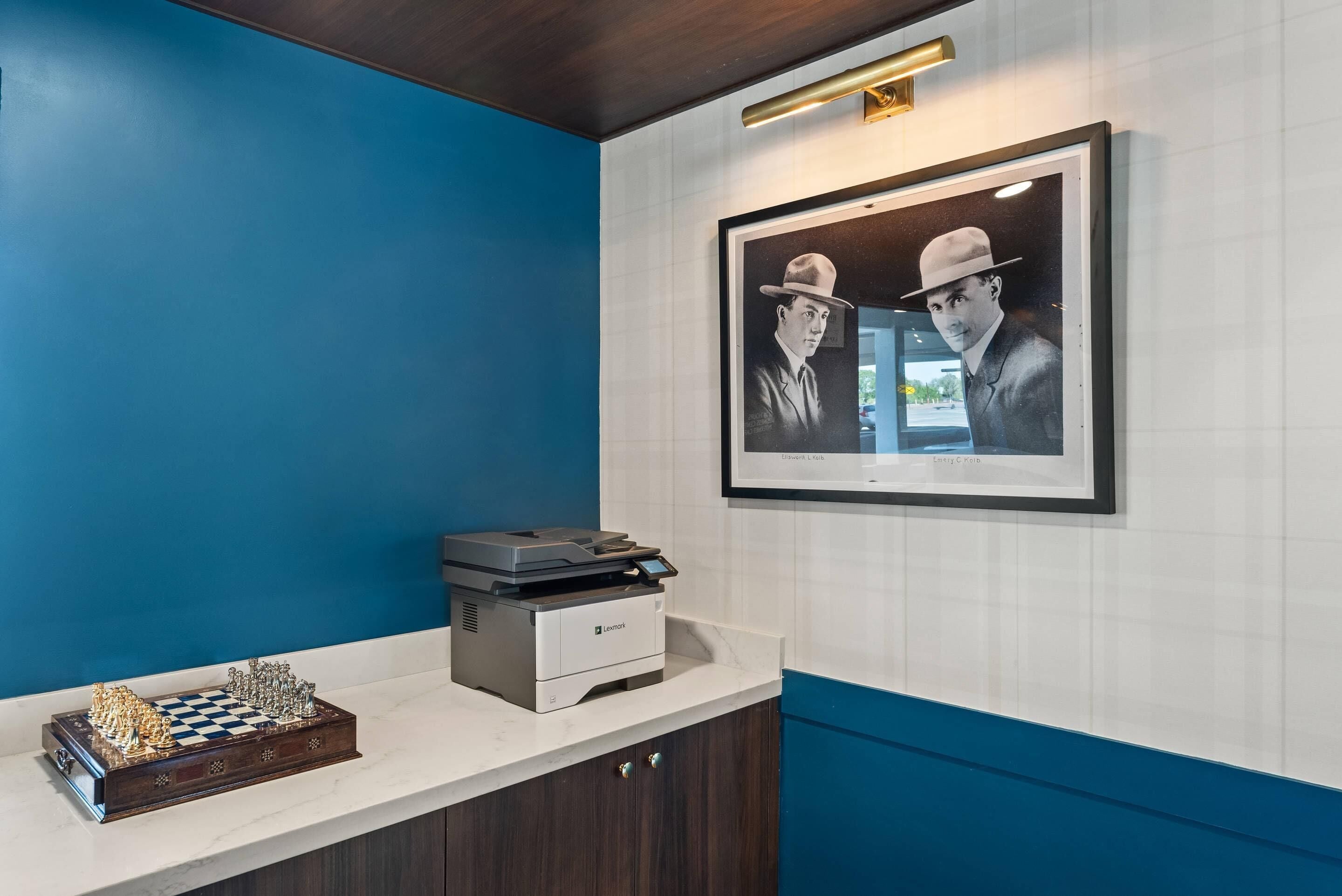 Un área de recepción con un tablero de ajedrez, una impresora y fotografías enmarcadas en la pared.