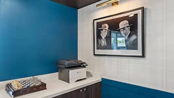 Un área de recepción con un tablero de ajedrez, una impresora y fotografías enmarcadas en la pared.