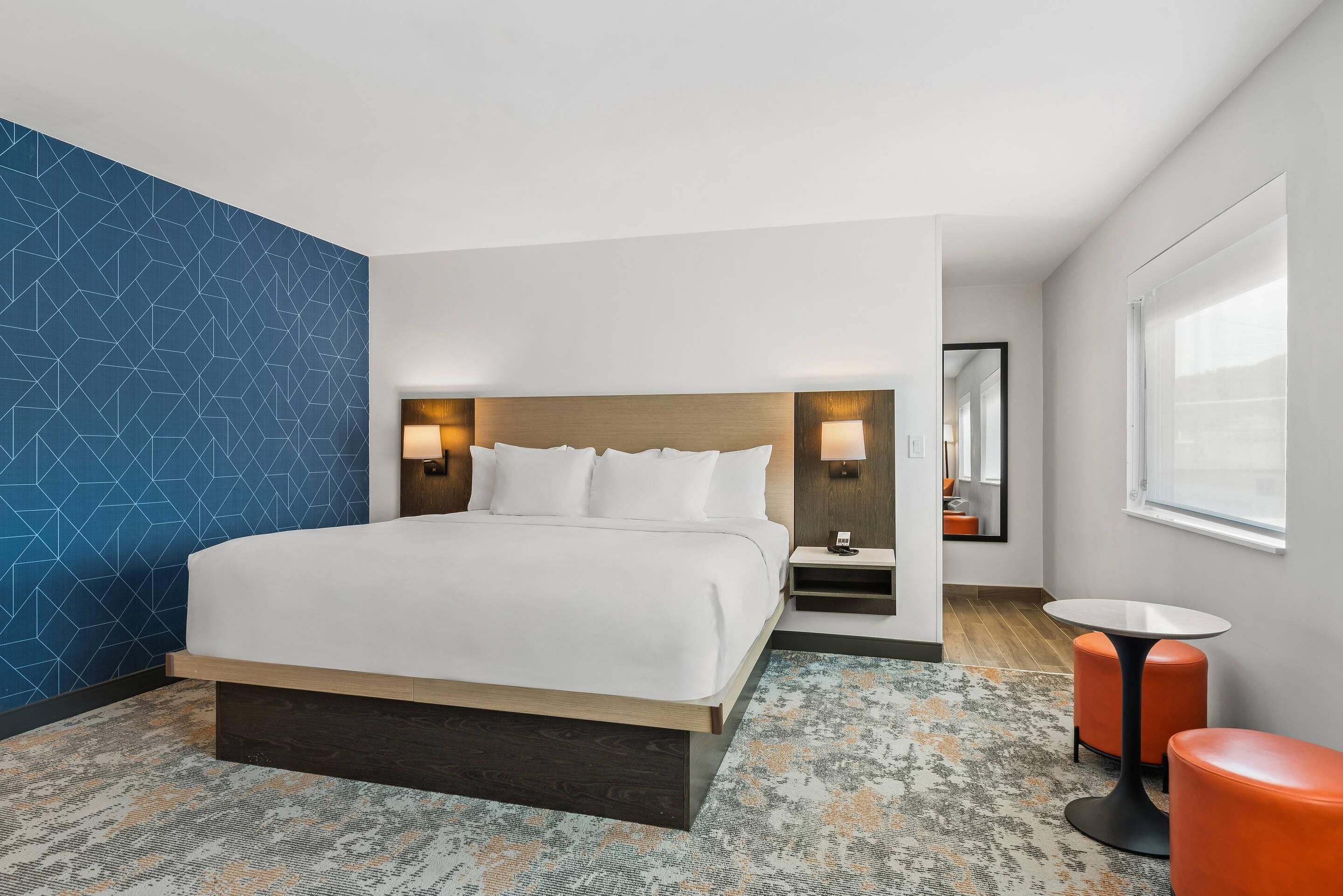 A hotel room with a large bed, bedside tables, a small round table, and a mirror.