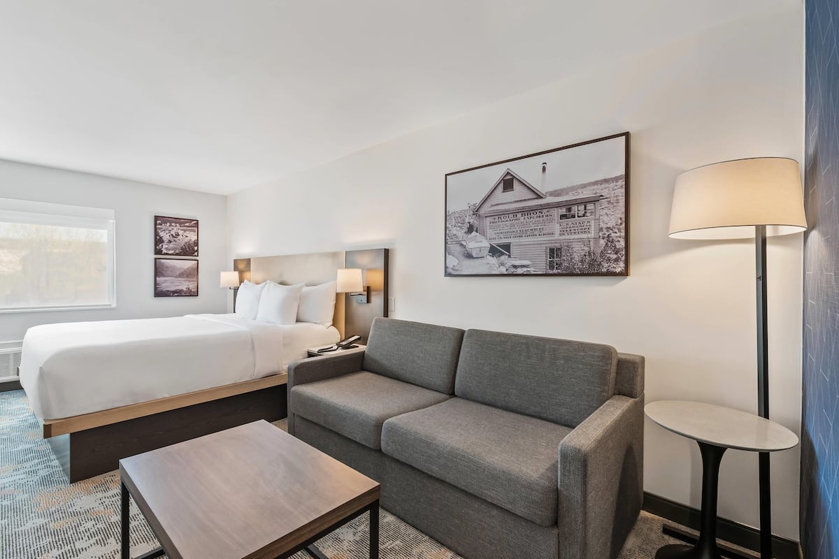 Ein Hotelzimmer mit Bett, Sofa, kleinem Tisch, Lampe und einem gerahmten Bild an der Wand.