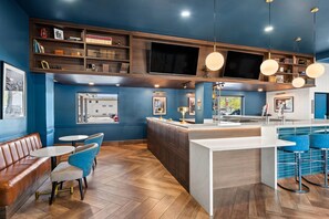 A modern kitchen with a large island, bar stools, and a seating area with a brown leather bench and blue chairs. - The Ellsworth Hotel, an Ascend Collection Hotel (Williams)