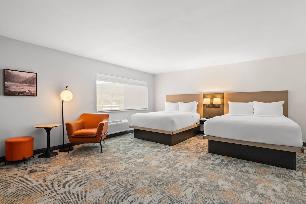Ein Hotelzimmer mit zwei Betten, einem Sessel, einem kleinen Tisch, einer Lampe und einem Bild an der Wand.