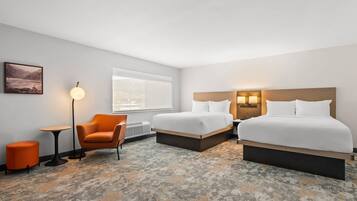 A hotel room with two beds, a chair, a small table, a lamp, and a picture on the wall.