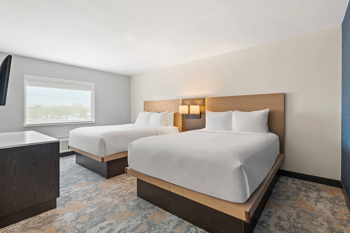 Ein Hotelzimmer mit zwei Betten, einem Schreibtisch und einem Fenster mit Jalousien.