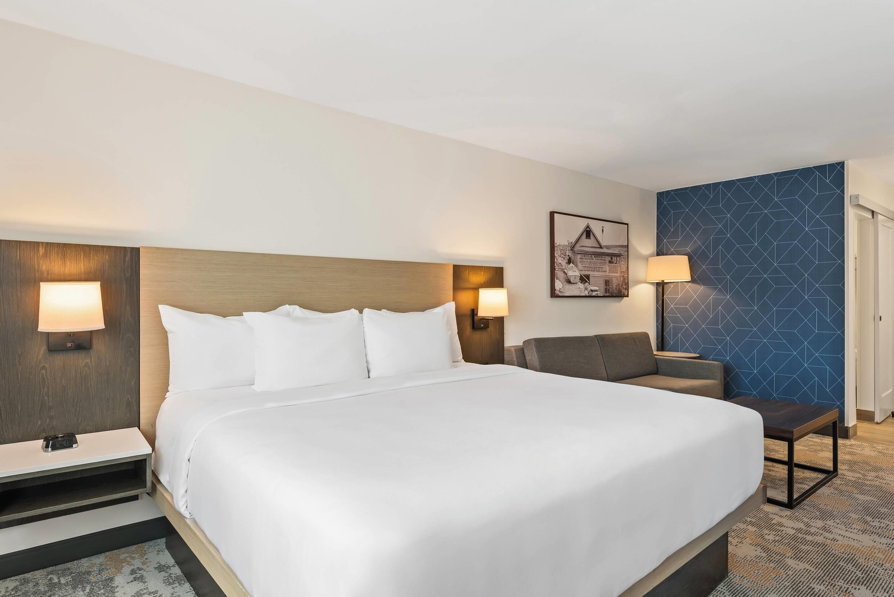 A hotel room with a large bed, bedside tables, a chair, and a lamp.