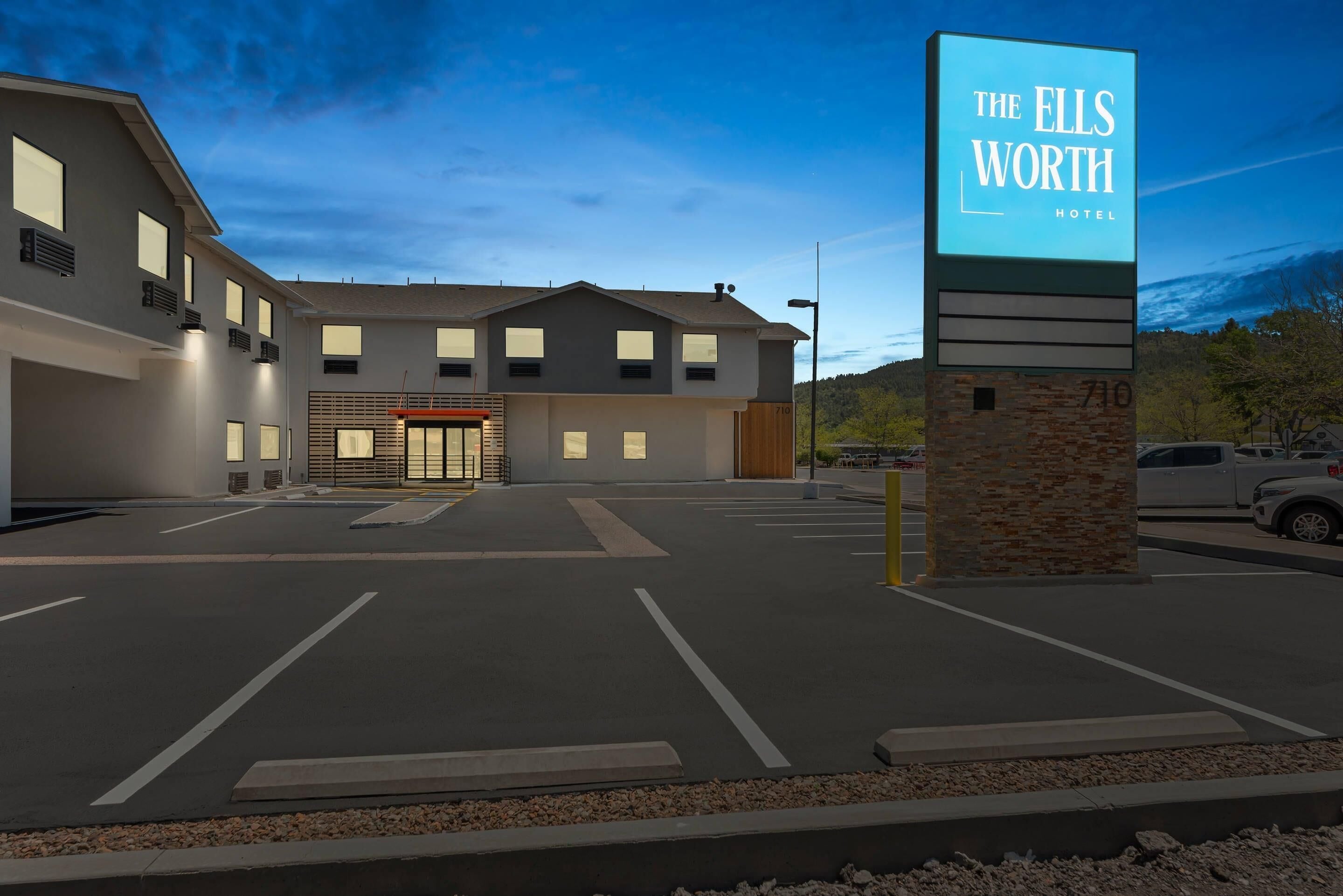 A modern hotel with a prominent sign, a parking lot, and a building facade with multiple windows.