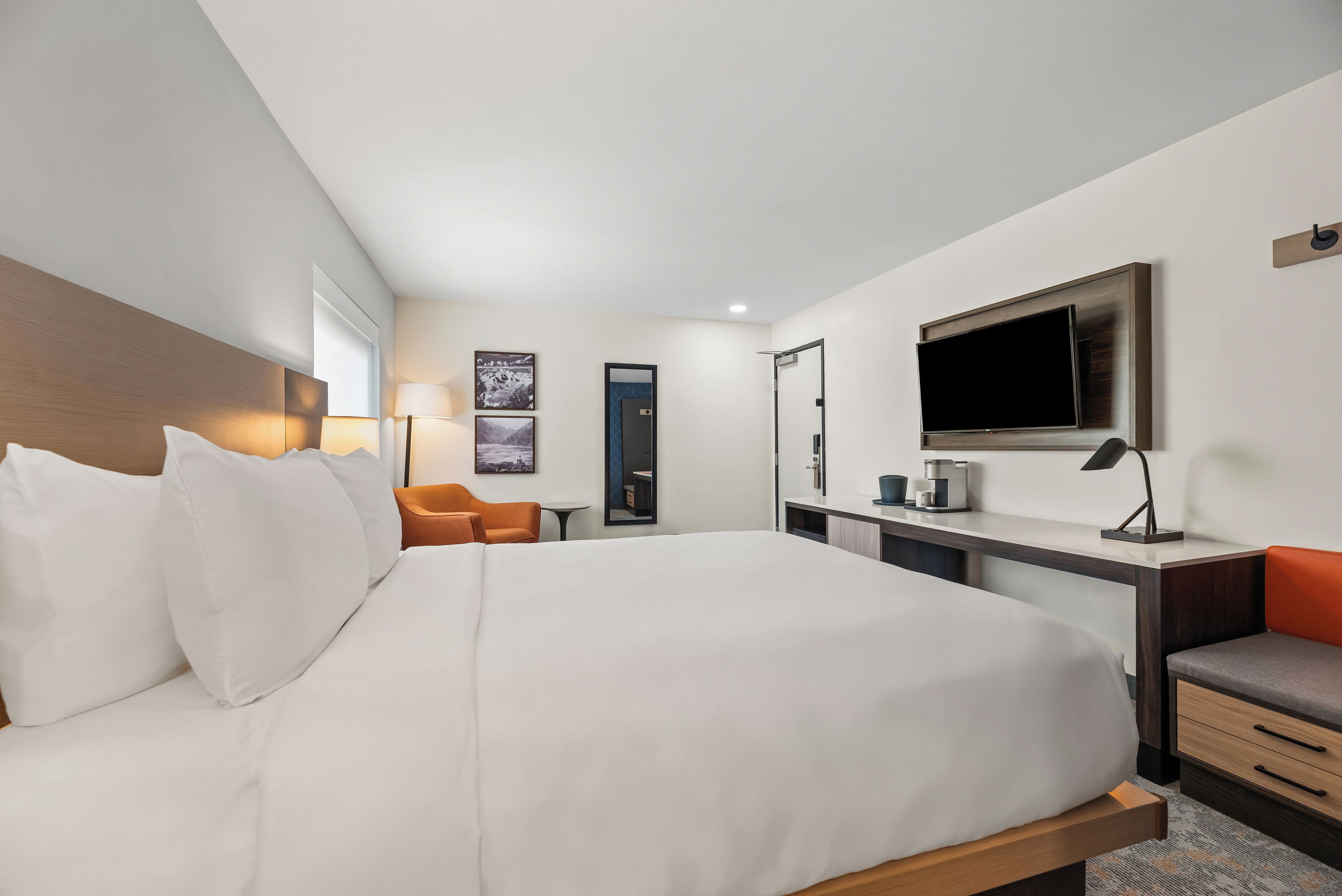 Een moderne hotelkamer met een groot bed, een bureau met een flatscreen-televisie, een stoel en een klein tafeltje.