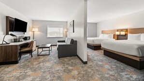 Een hotelkamer met een bureau, twee bedden, een bank, een televisie en een raam.